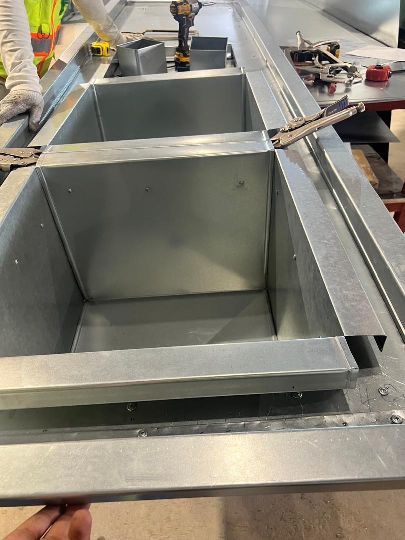 Worker assembling a galvanized steel duct section on a workshop table